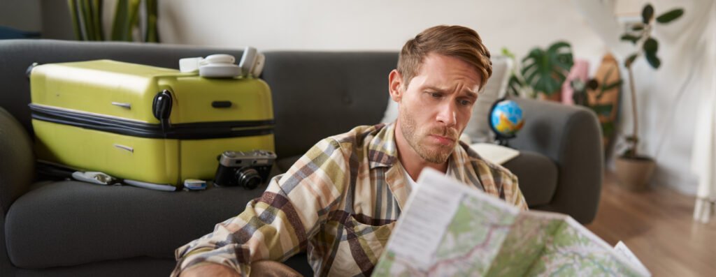 Renew Your Visa in Spain 6 portrait man with concerned puzzled face looking map frowning while studying route sitting with suitcase going vacation