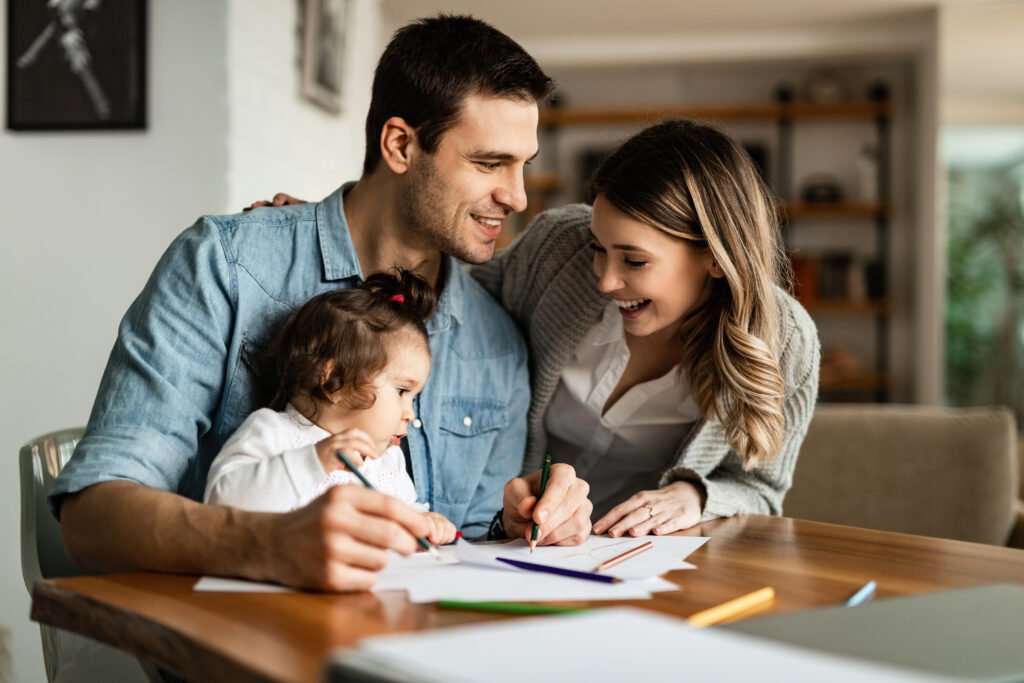 young happy parents enjoying coloring with their small daughter home